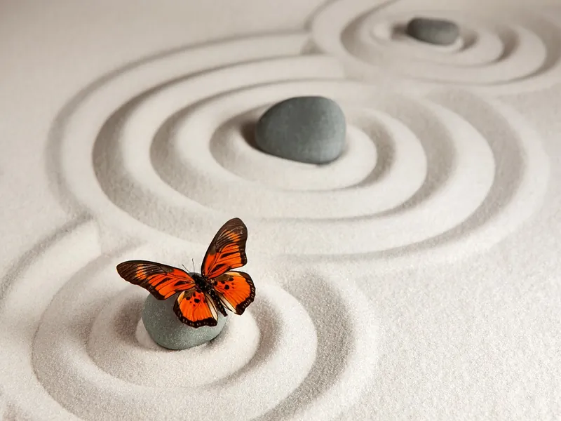 Image d'une zone de méditation zen avec trois pierres sur du sable et papillon orangé